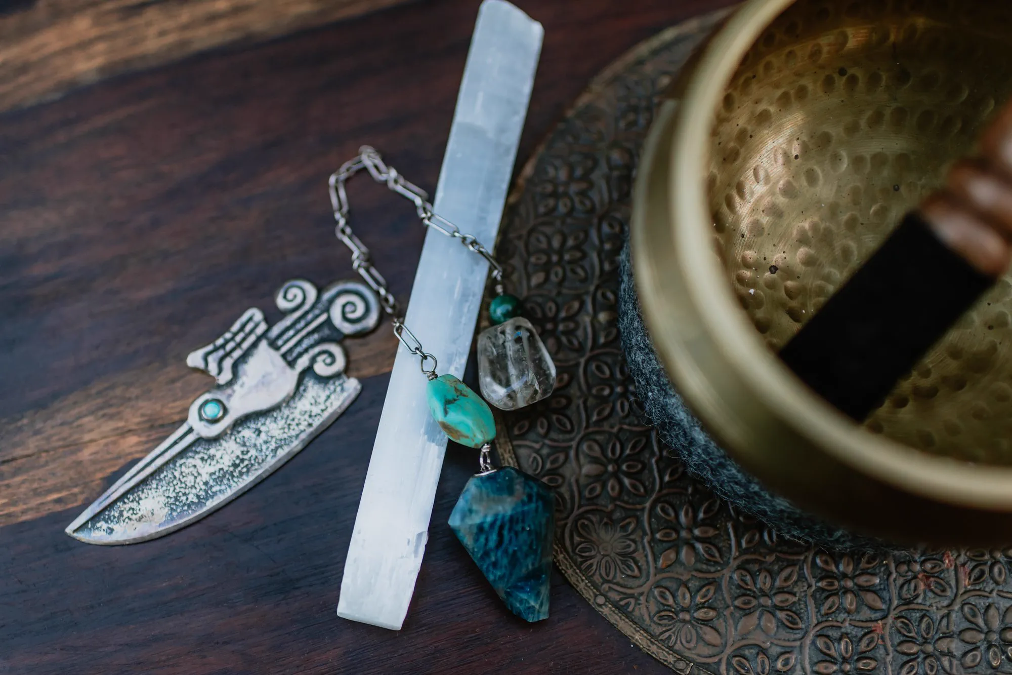 A ritual blade, selenite, a kyanite pendant and a bowl arranged on dark wood.