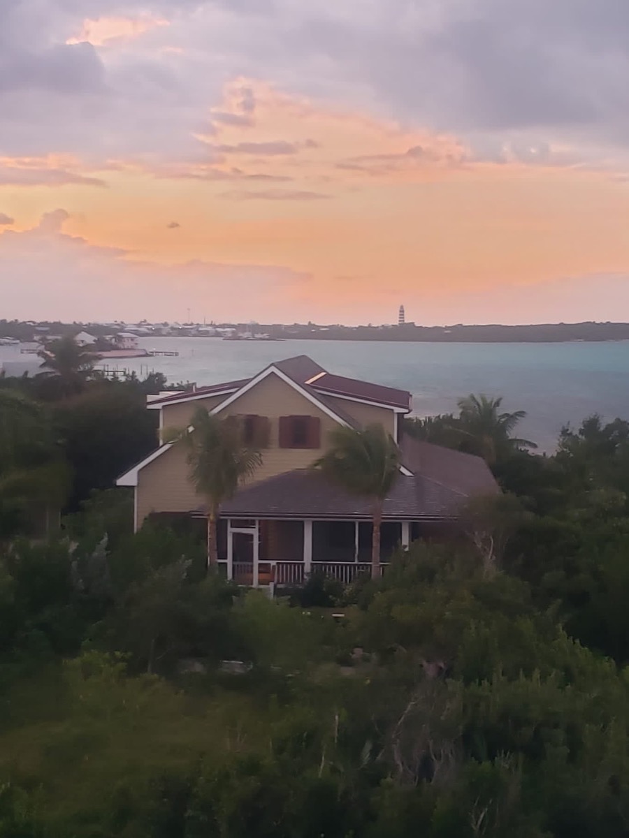 The house at golden hour seen from above, the Sea of Abaco and the Hope Town lighthouse on the horizon.