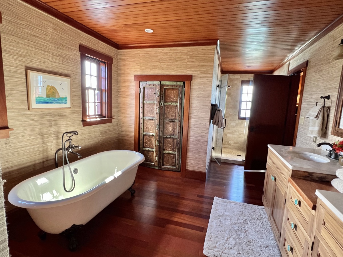 A freestanding clawfoot soaking tub on dark hardwood beside an antique carved door and glass walk-in shower.