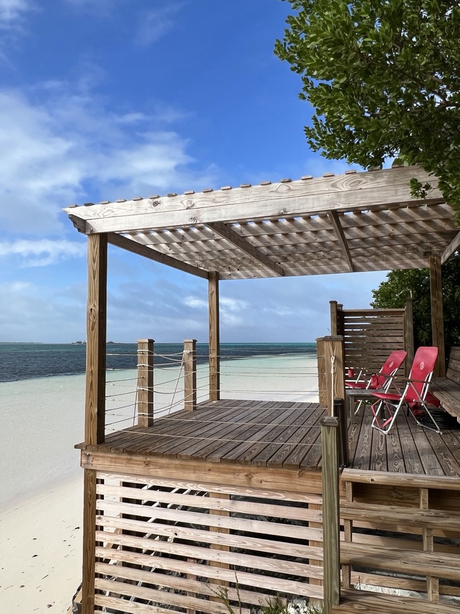 A covered beach cabana with cushioned loungers on the deck, white sand and the turquoise Sea of Abaco beyond.