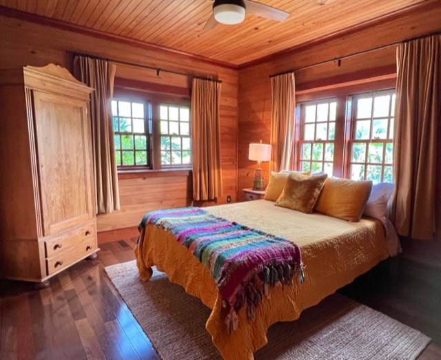 The guest bedroom with gold linens, a pine armoire and four garden-facing windows.