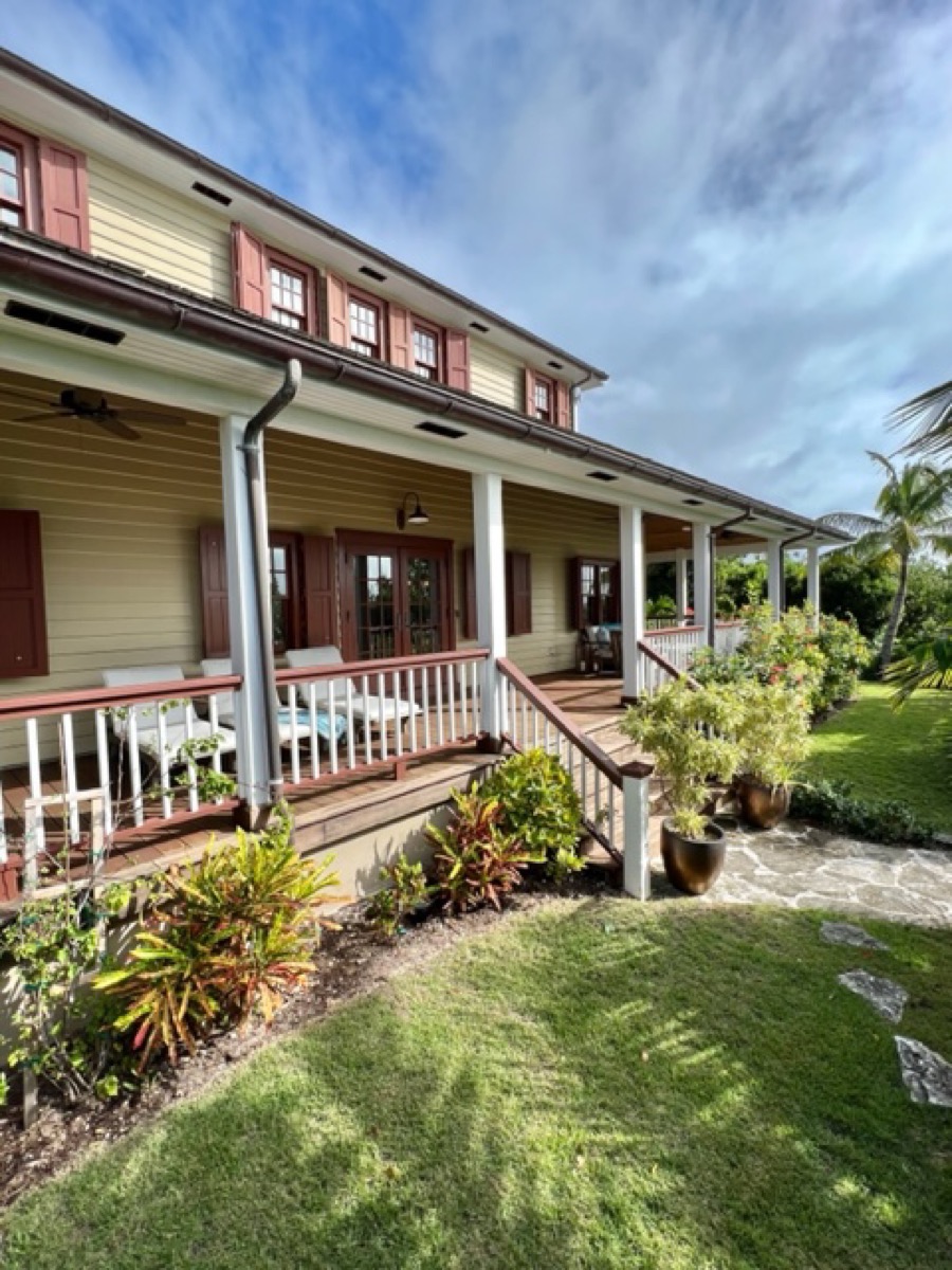 The wraparound porch and tropical garden from the side, a stone path leading through lush plantings.
