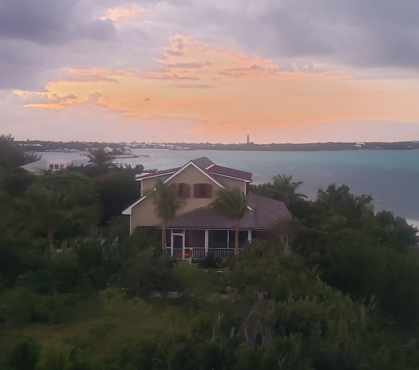 The property at golden hour, the house framed by palms above the calm pink-lit Sea of Abaco.