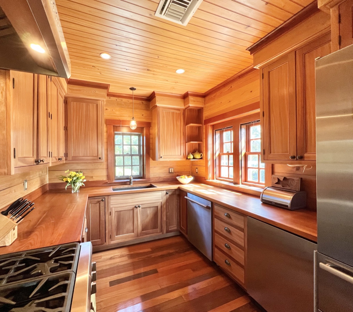 A full chef kitchen with warm wood cabinetry, butcher-block counters, stainless appliances and a garden window.