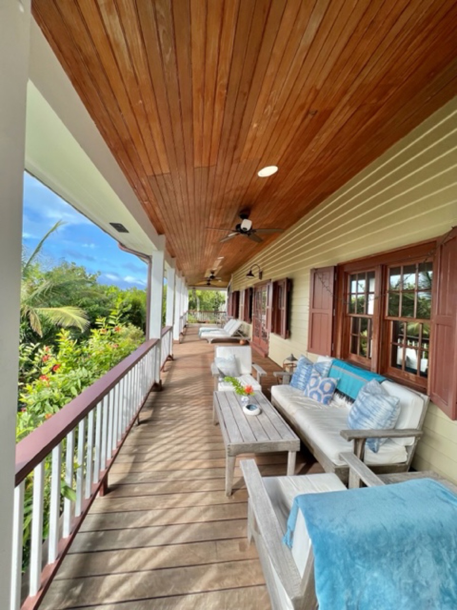 The long covered veranda with cushioned sofas, a coffee table and garden views beyond the white railing.
