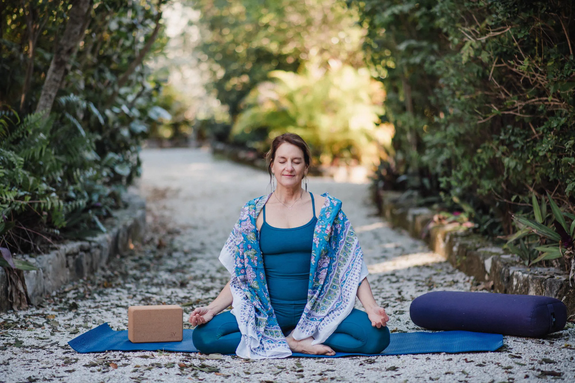 A guest seated in meditation on a garden path, supported by a bolster and block.